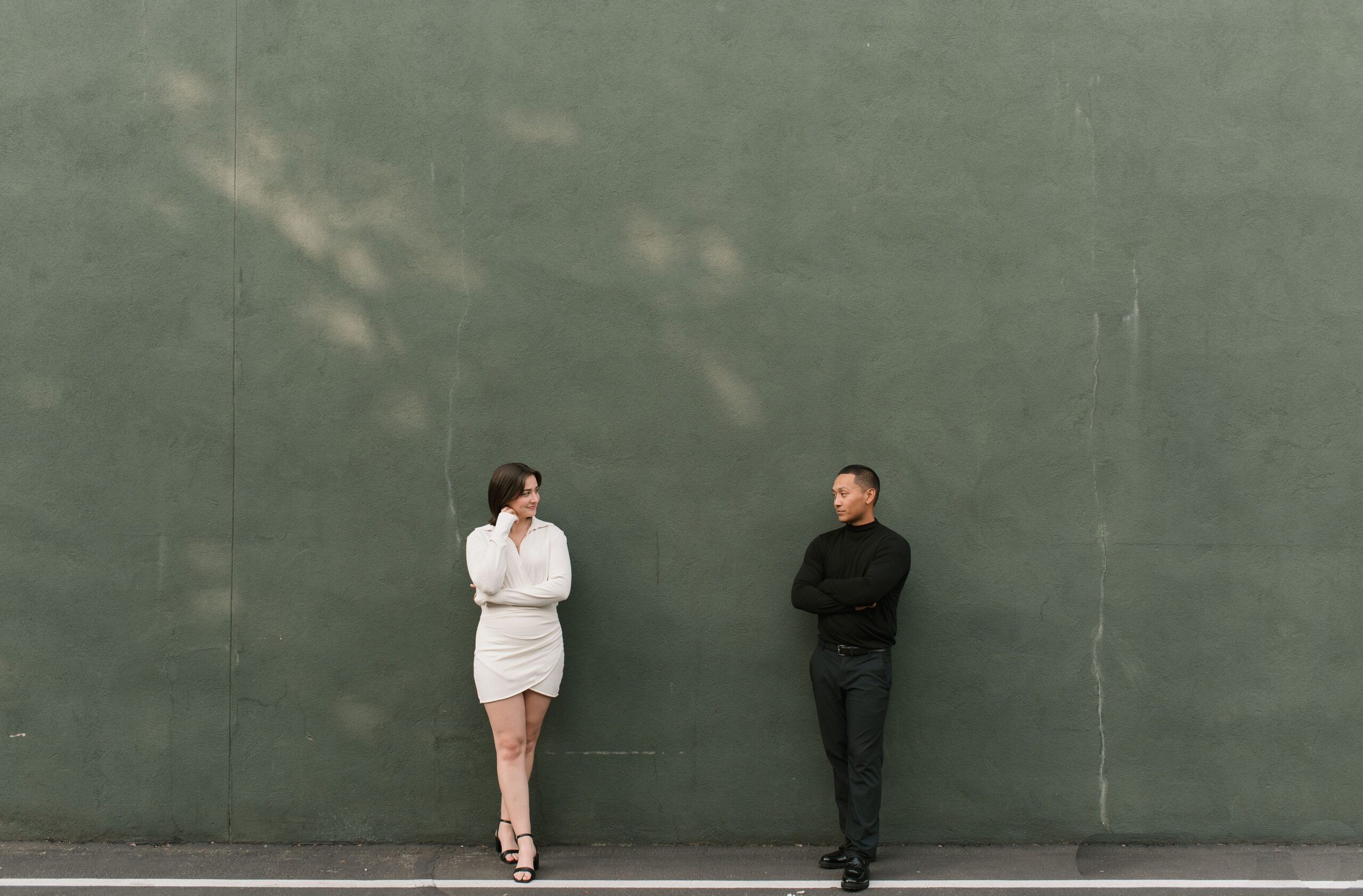 couple looking at each other against a green wall at editorial couple photoshoot 