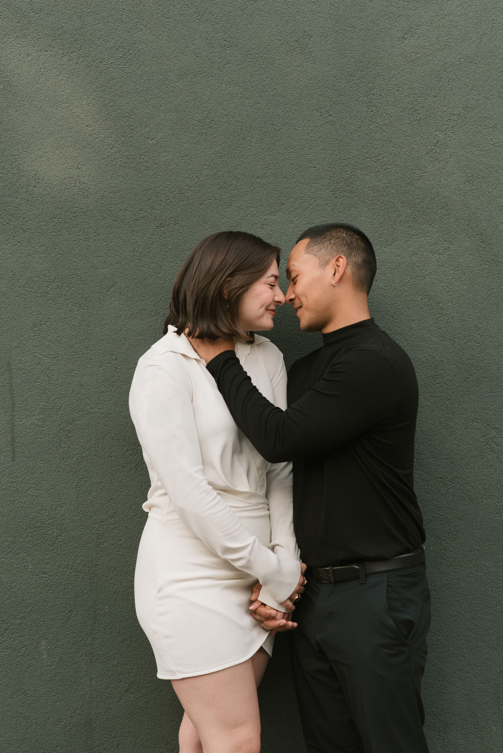 couple standing next to the green wall holding each other at editorial couple photoshoot 