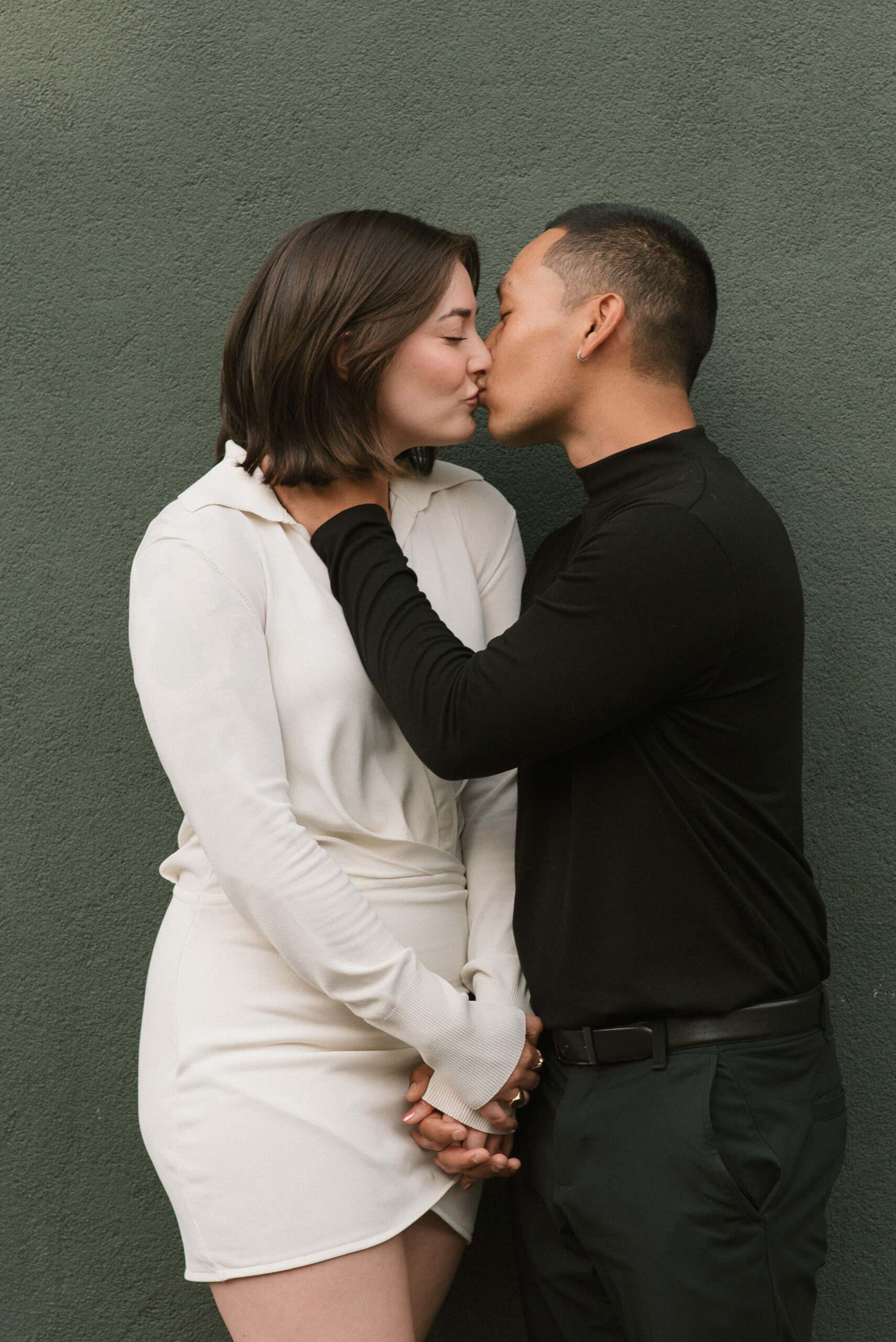 couple standing next to the green wall kissing at editorial couple photoshoot 