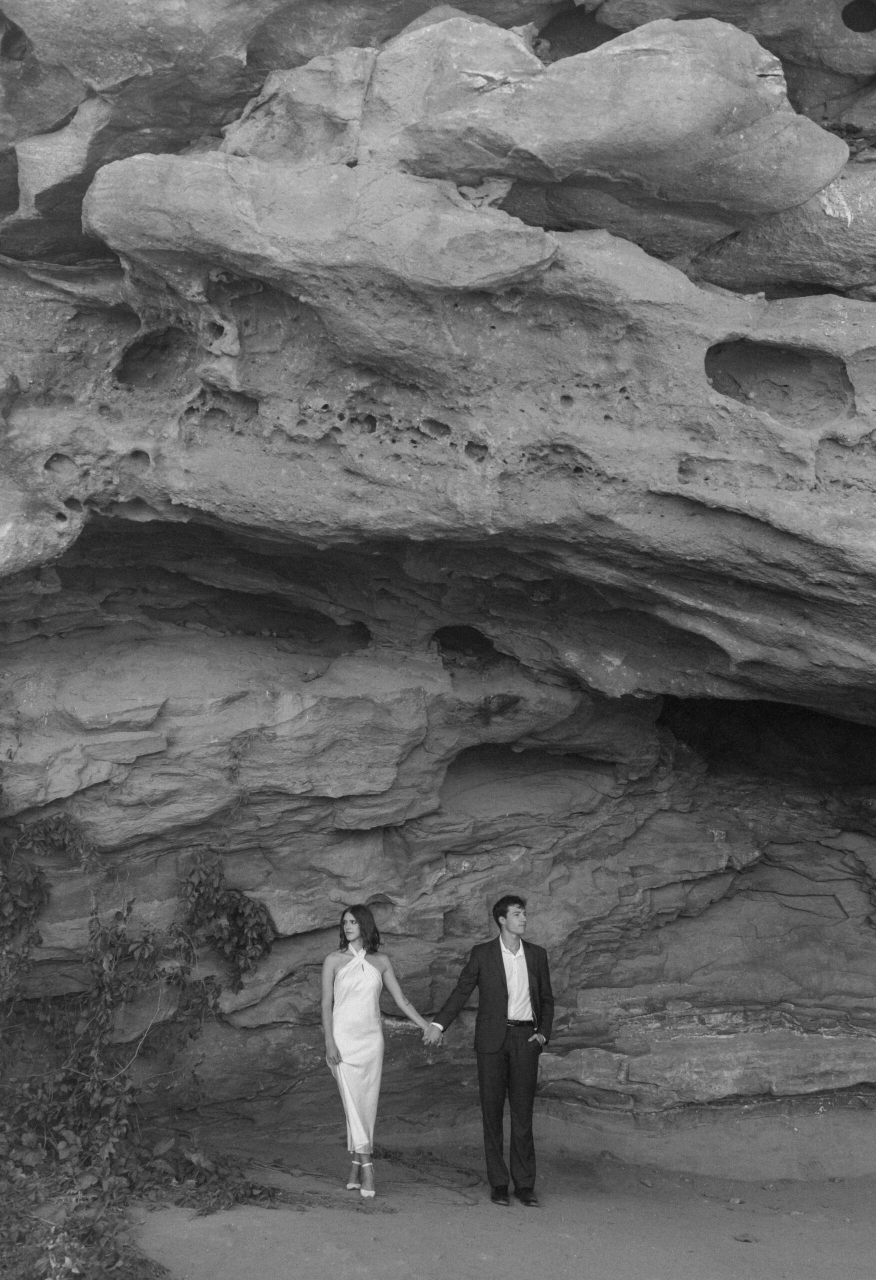 bridal couple in front of rock wall holding hands 