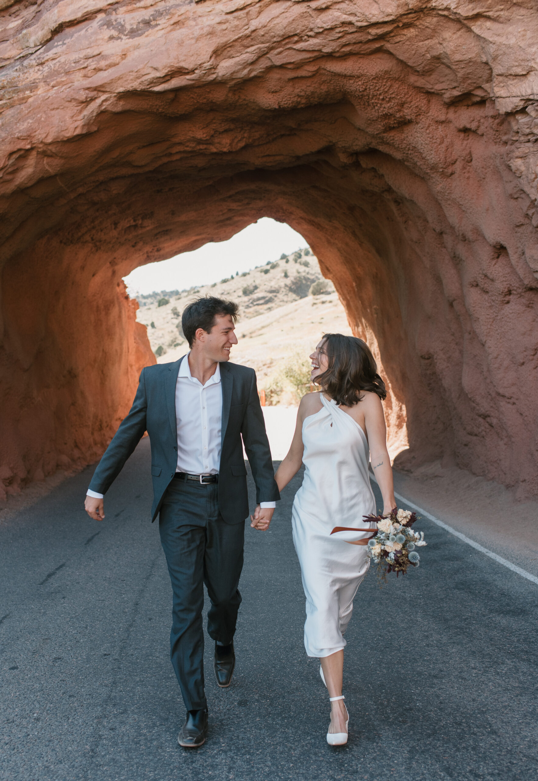 bridal couple running on the road with a red rock arch behind them at colorado elopement 