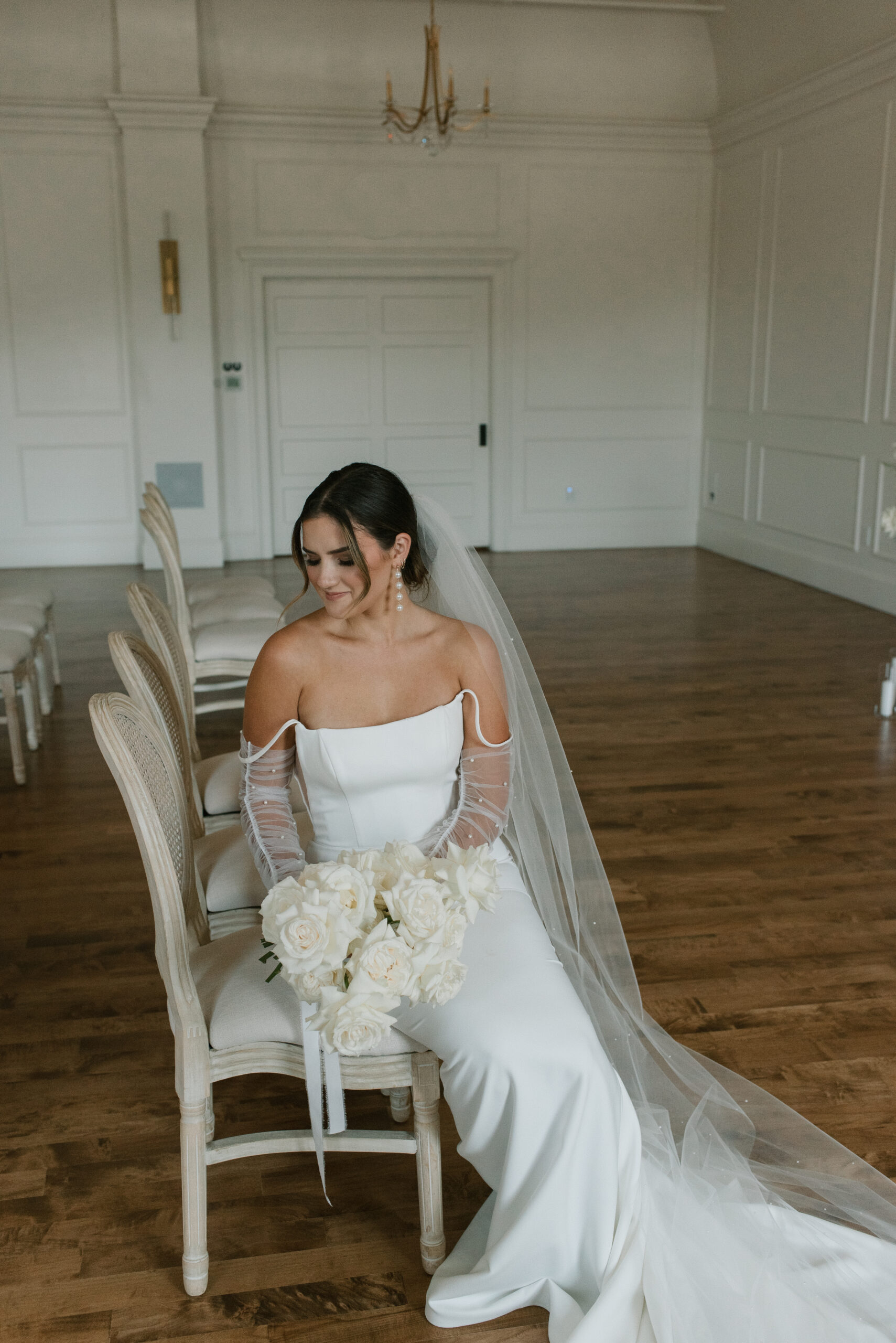 bride sitting on a chair holding white flower bouquet 