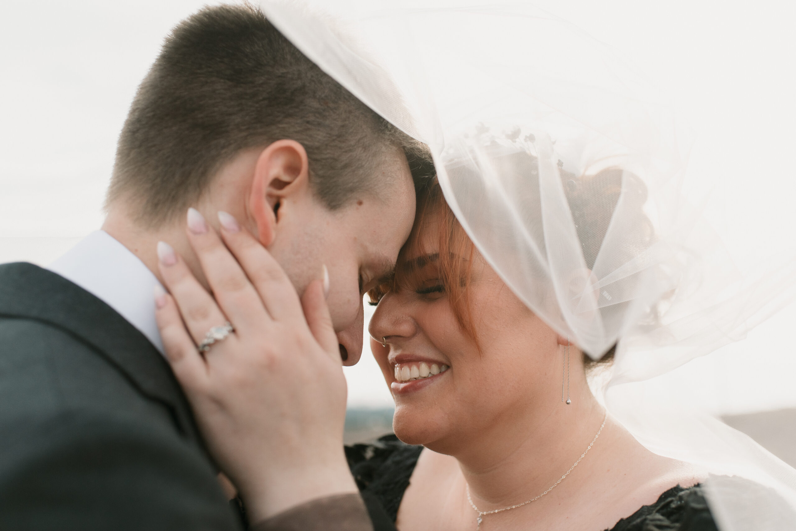 bride and groom smiling under wedding veil 