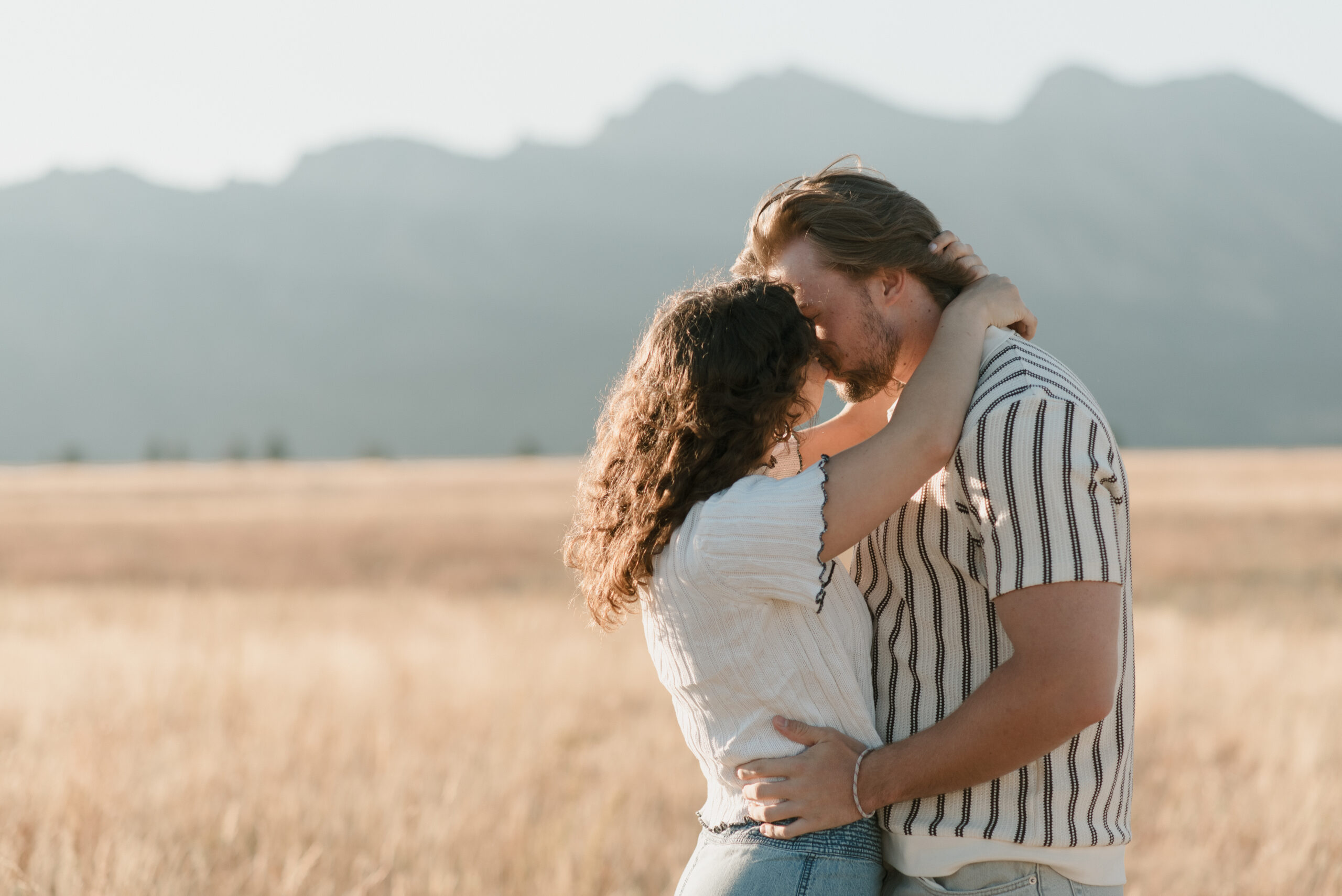 a couple standing in a grass field kissing during their couples photoshoot 