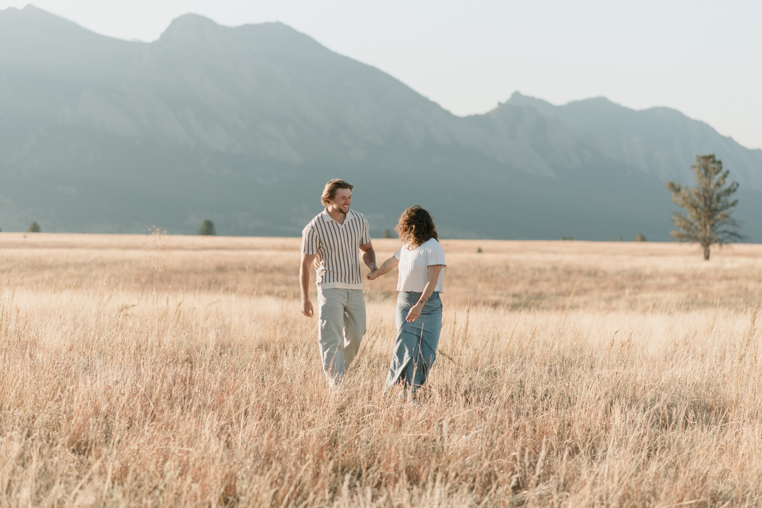 couple walking through the grass field together with mountains in the background during their couples photoshoot 