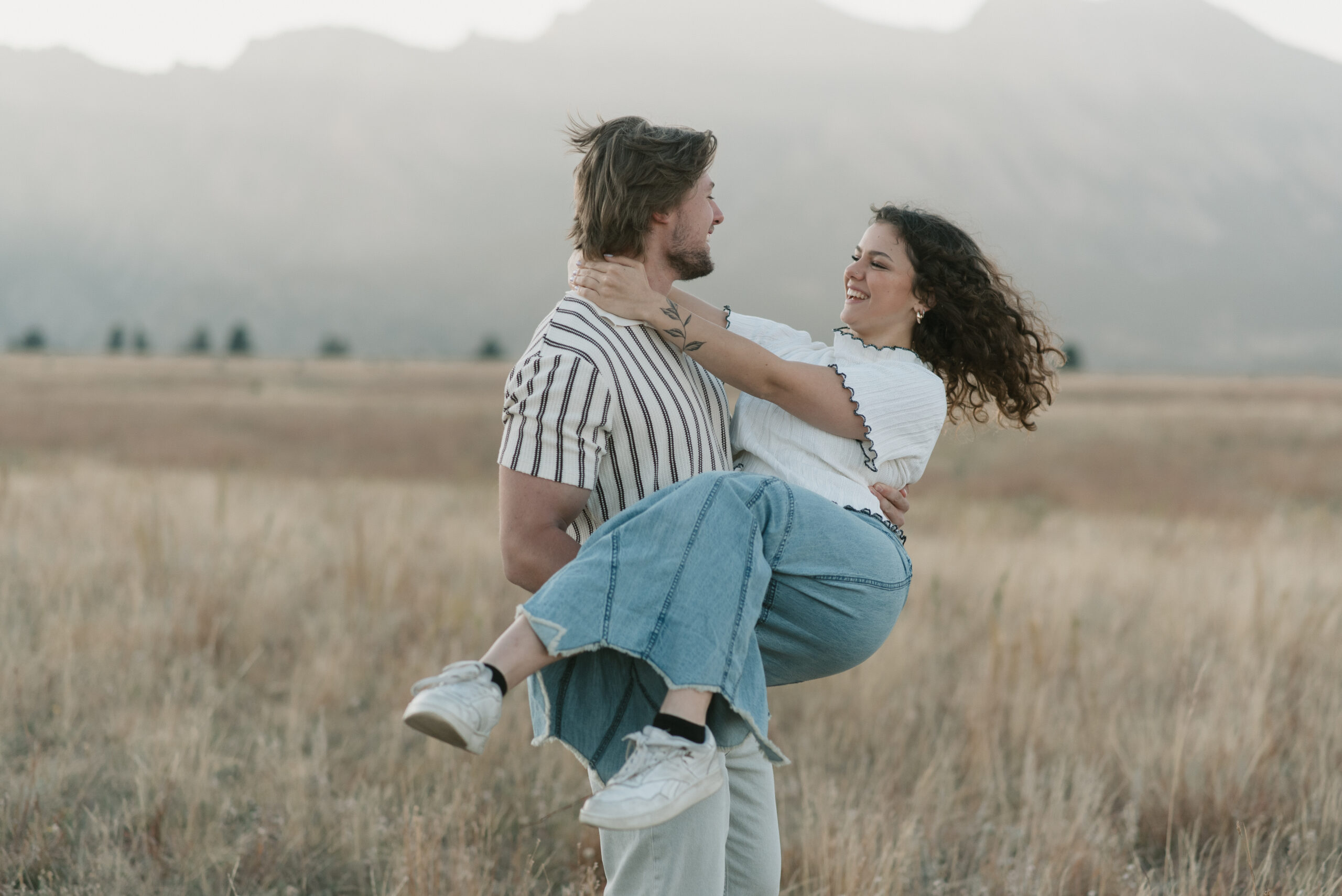 a man carrying a woman through a grass field during their couples photoshoot 