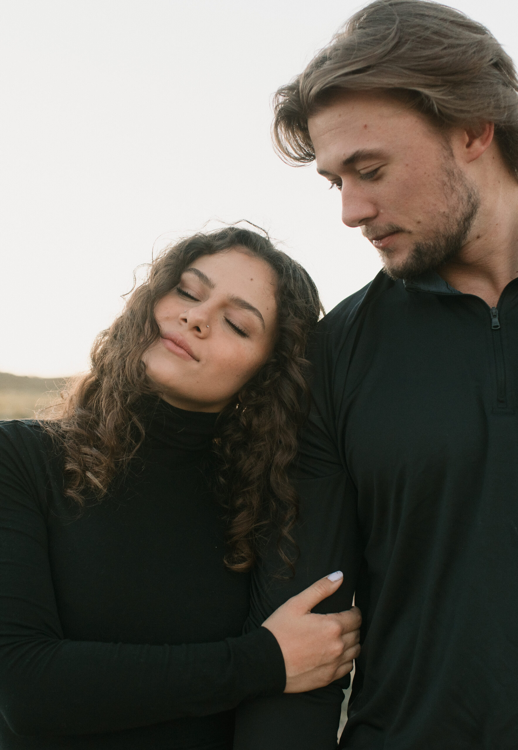 woman leaning head against man's shoulder as he looks down at her during a couples photoshoot 