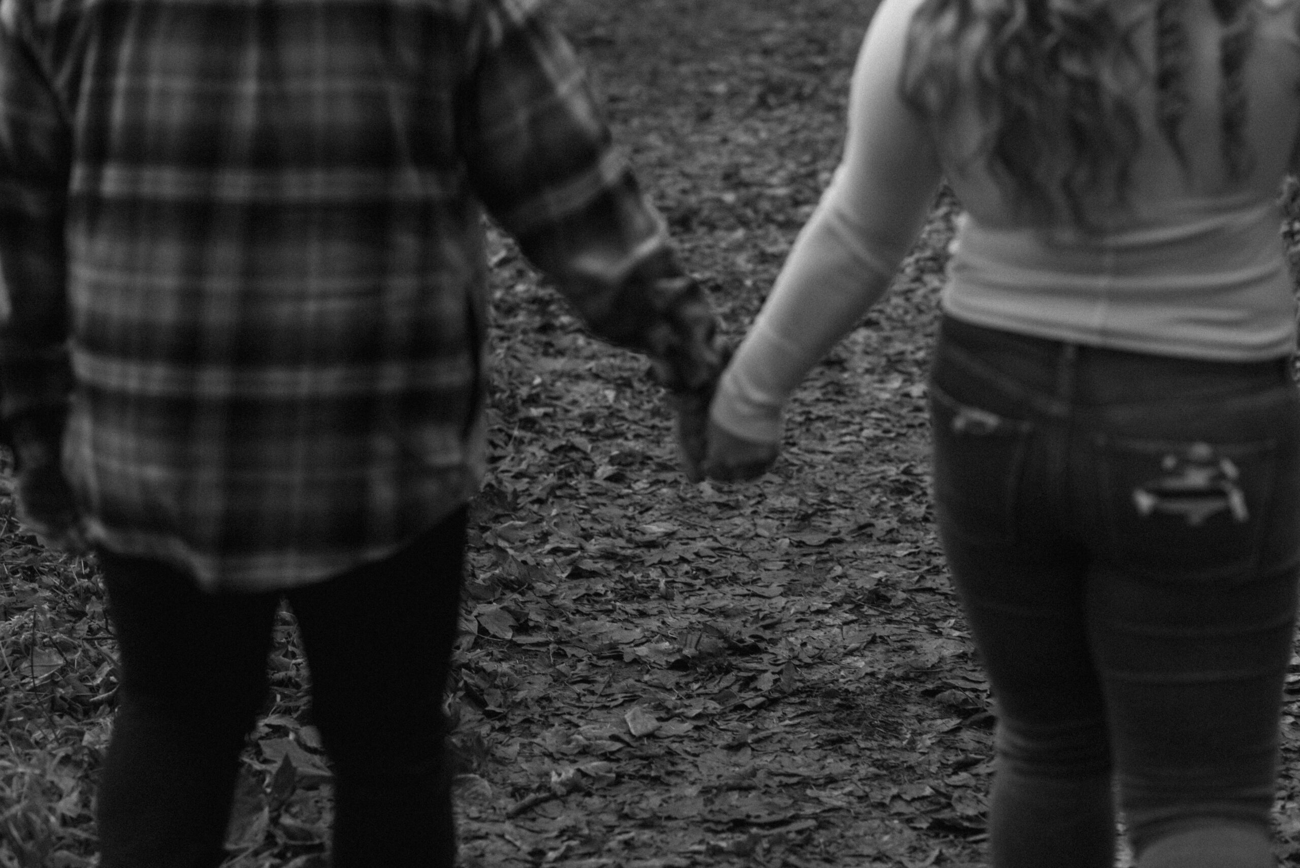 black and white blurry photo of a newly engaged couple holding hands and walking through the woods