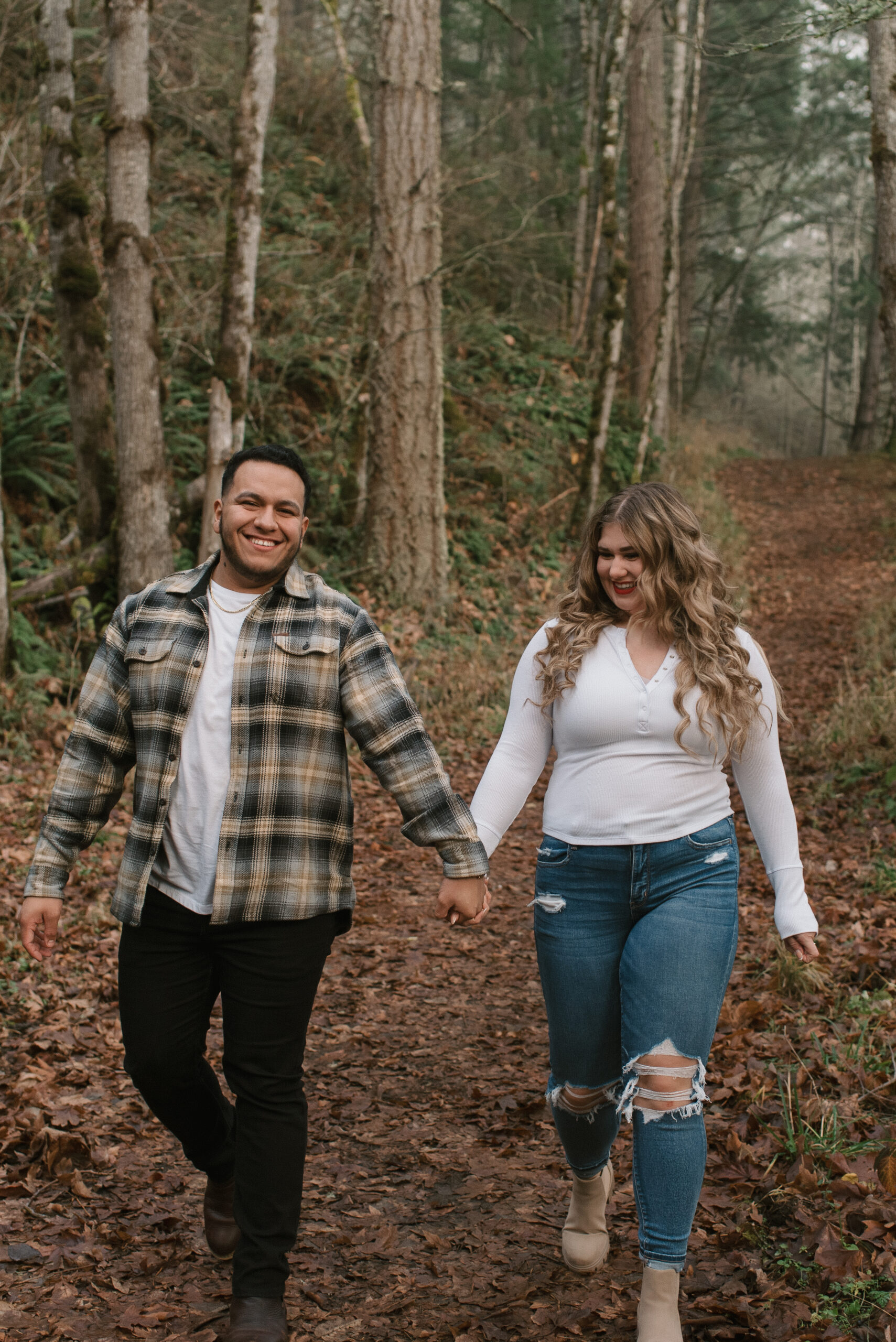 an engaged couple smiling and walking together in the forest captured by an Oregon engagement photographer 