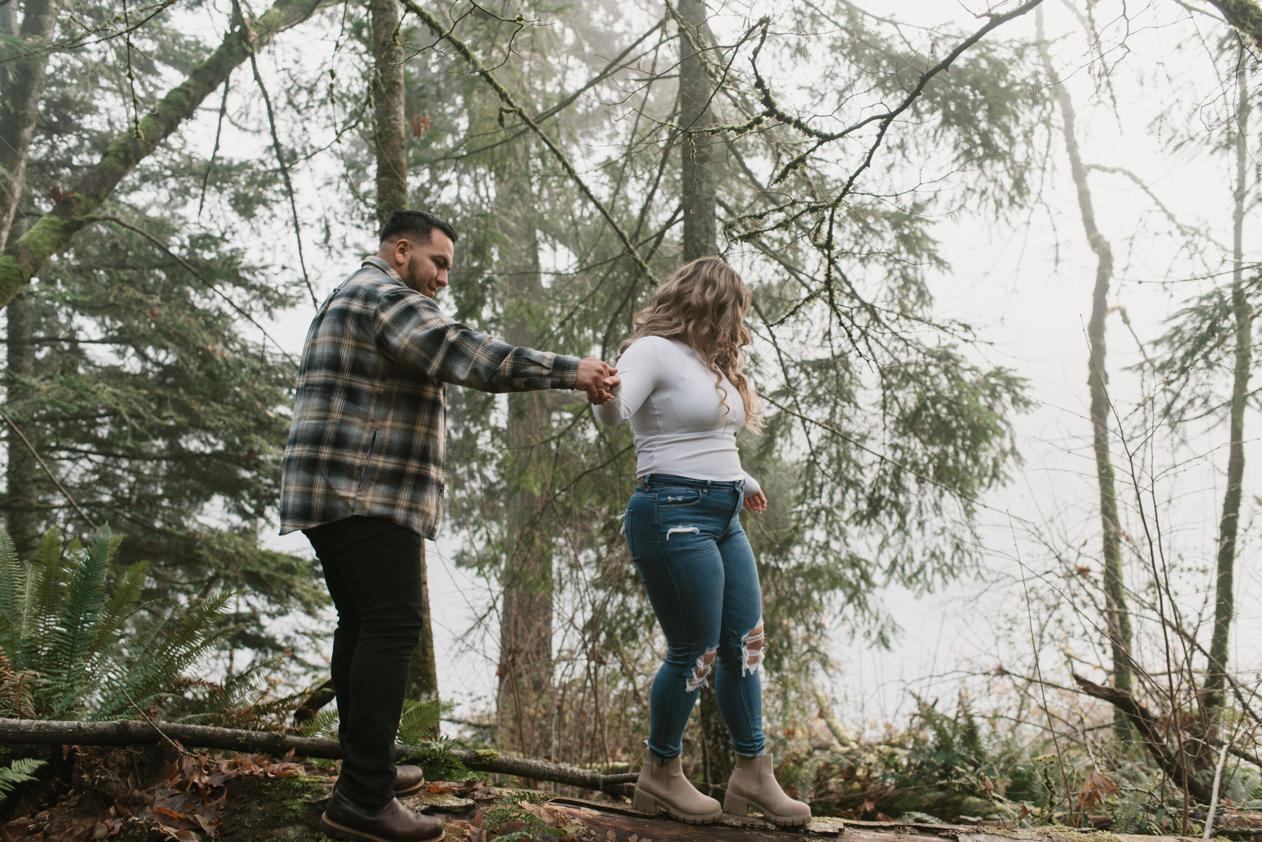 engaged couple walking on a log in the forest captured by an Oregon engagement photographer 
