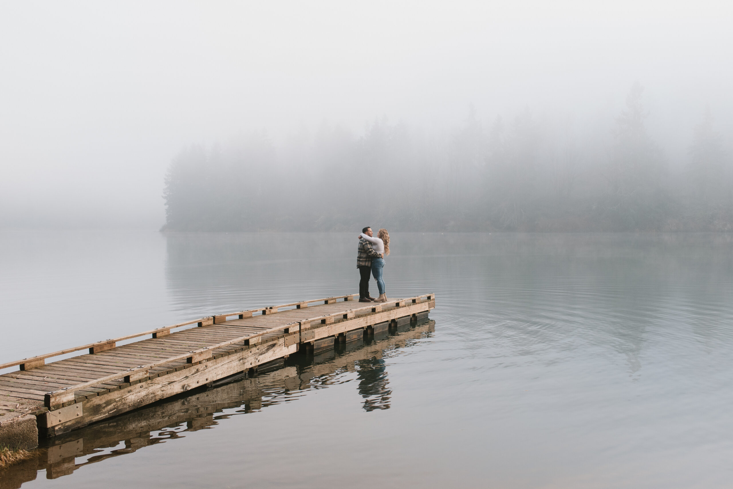 a couple holding each other at the end of the dock in the fog captured by an Oregon engagement photographer 