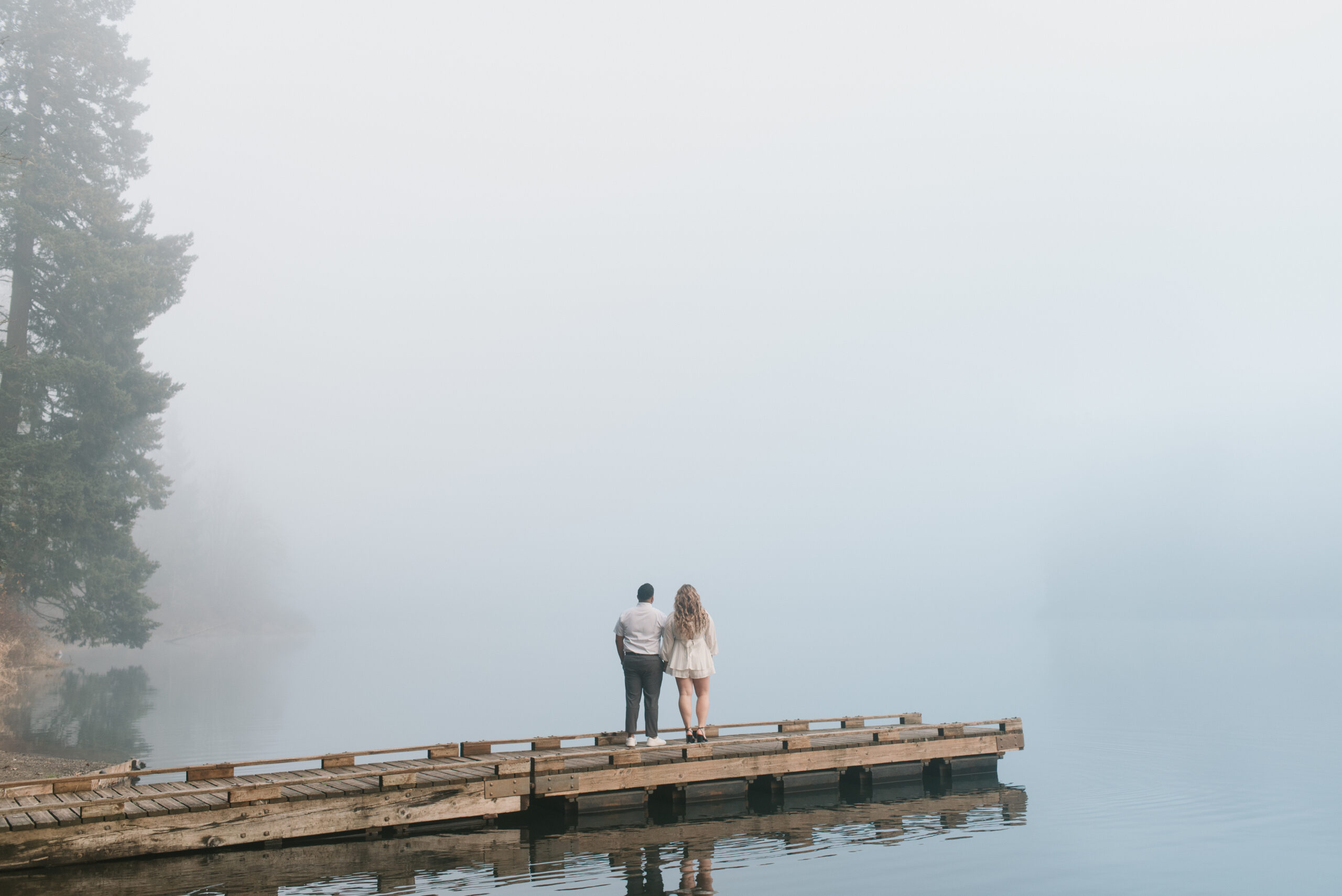 a couple standing side by side in the fog on a dock looking out into the water captured by an Oregon engagement photographer 