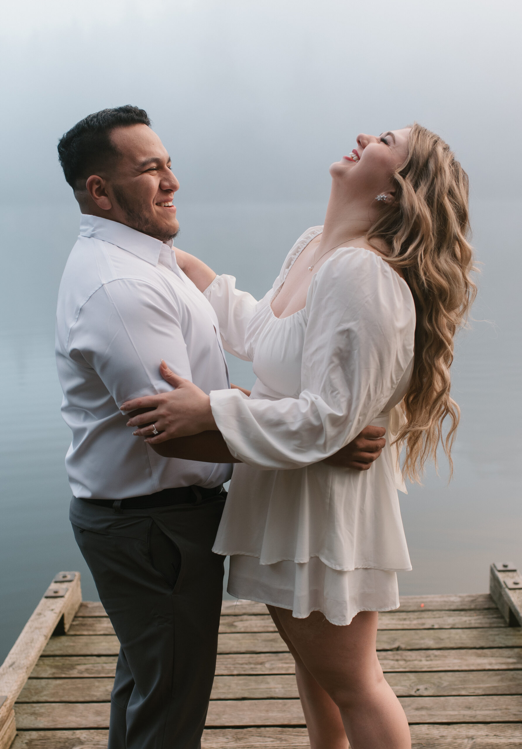 newly engaged couple laughing and holding each other in the fog on a dock