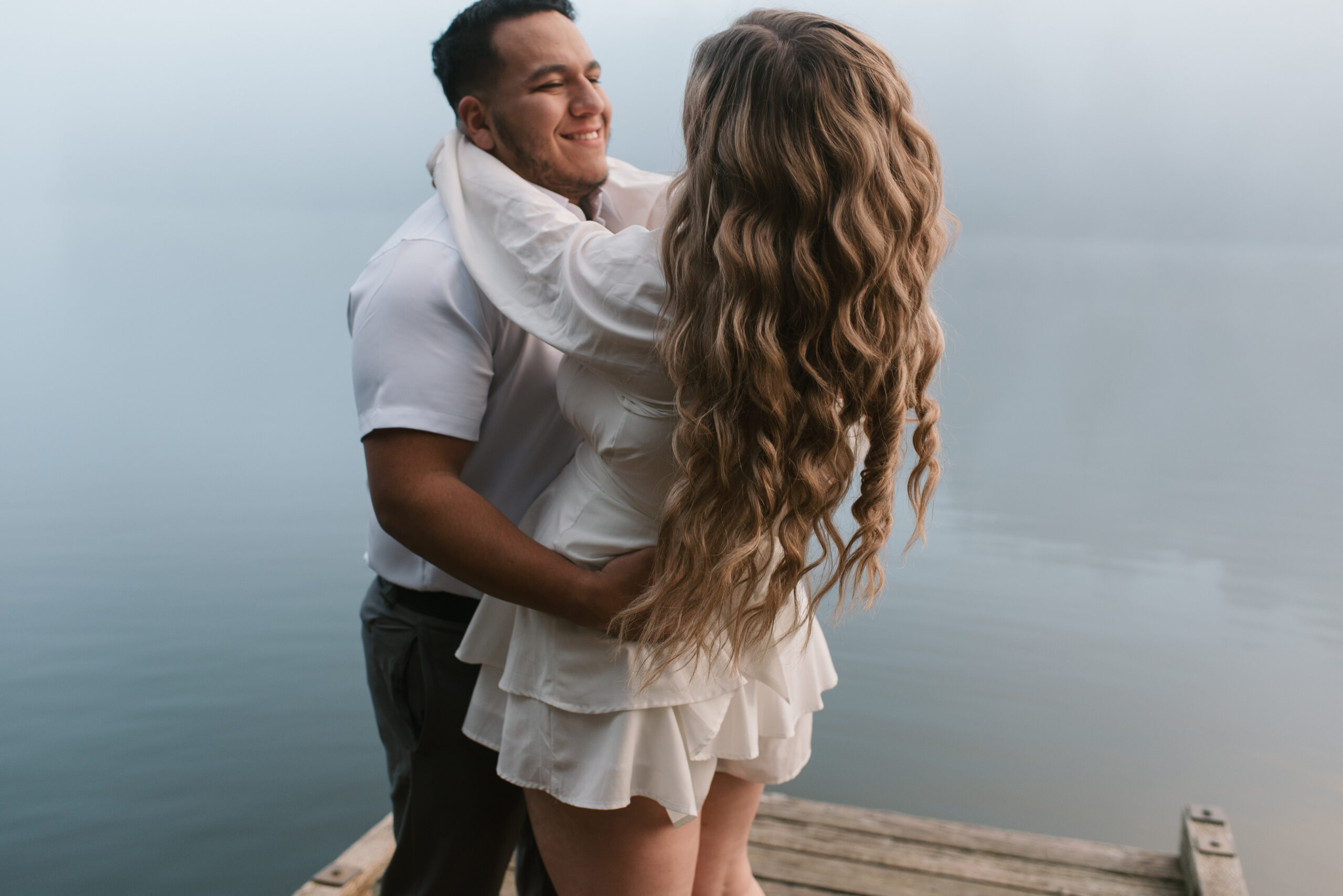 newly engaged couple holding each other and smiling on the dock 