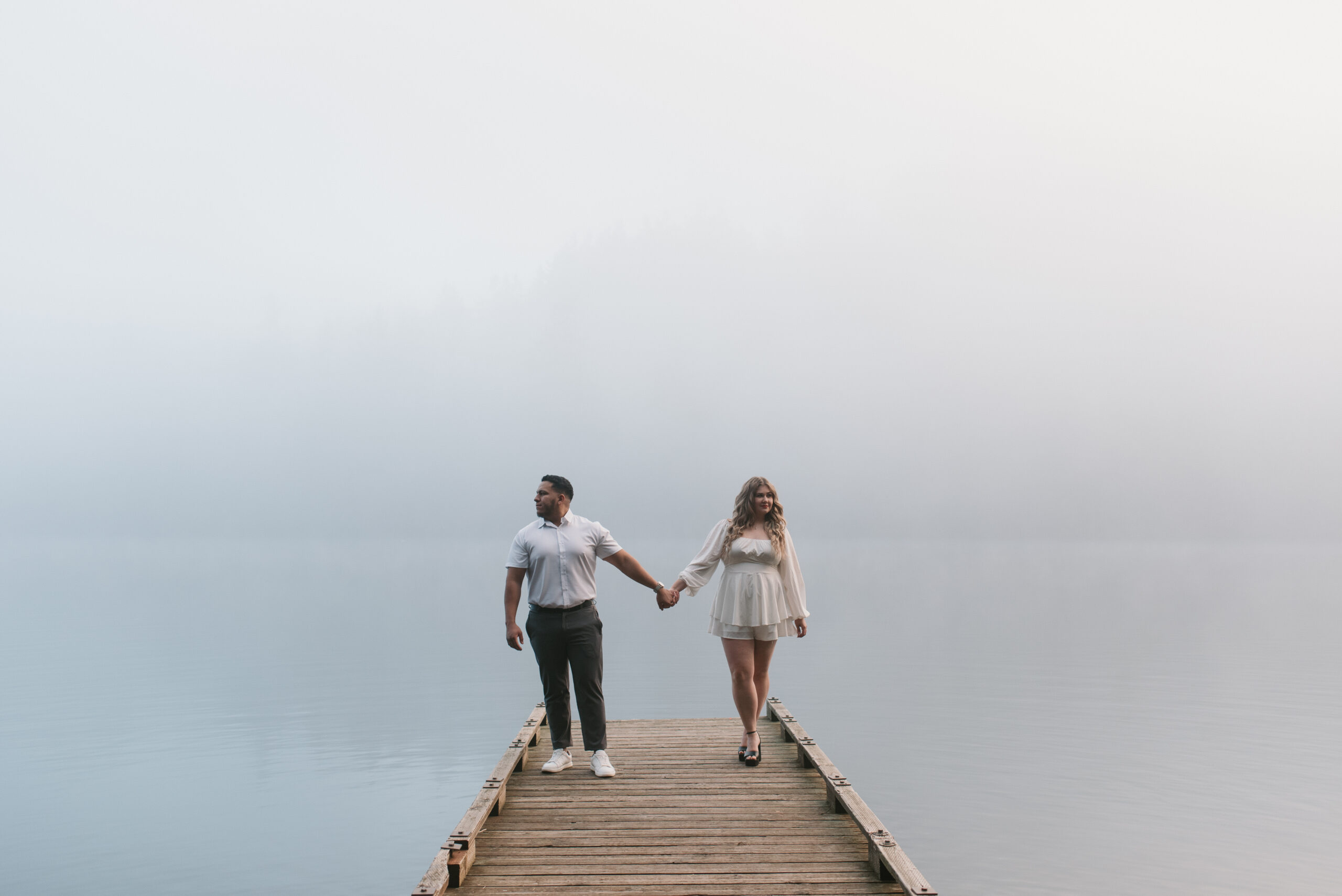 newly engaged couple holding hands and looking in opposite directions on the dock