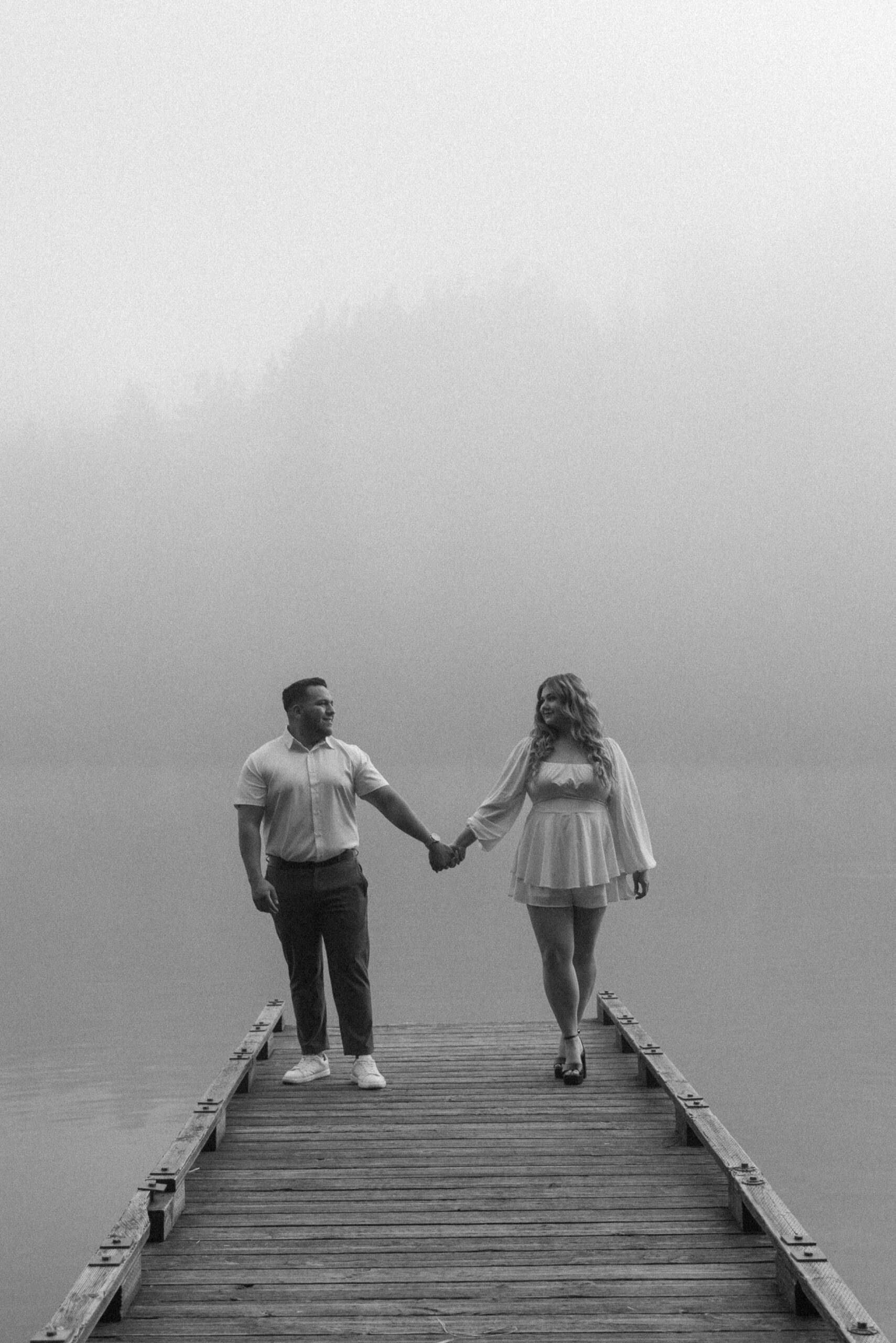 newly engaged couple holding hands on a dock in the fog