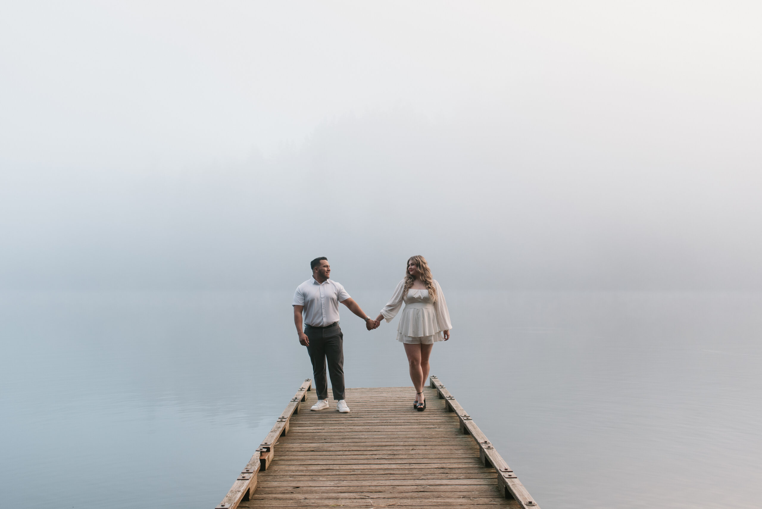 a couple holding hands on a dock while it is very foggy out captured by an Oregon engagement photographer 
