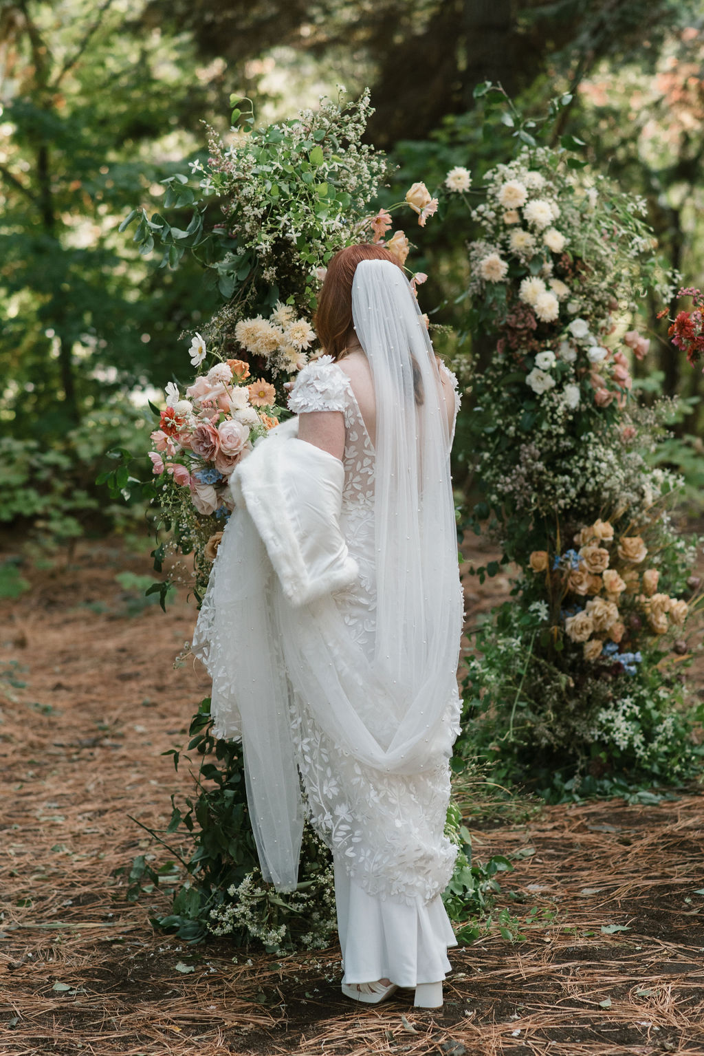 bride standing at the floral wedding arch with her bouquet in hand showing off her personalized wedding details 