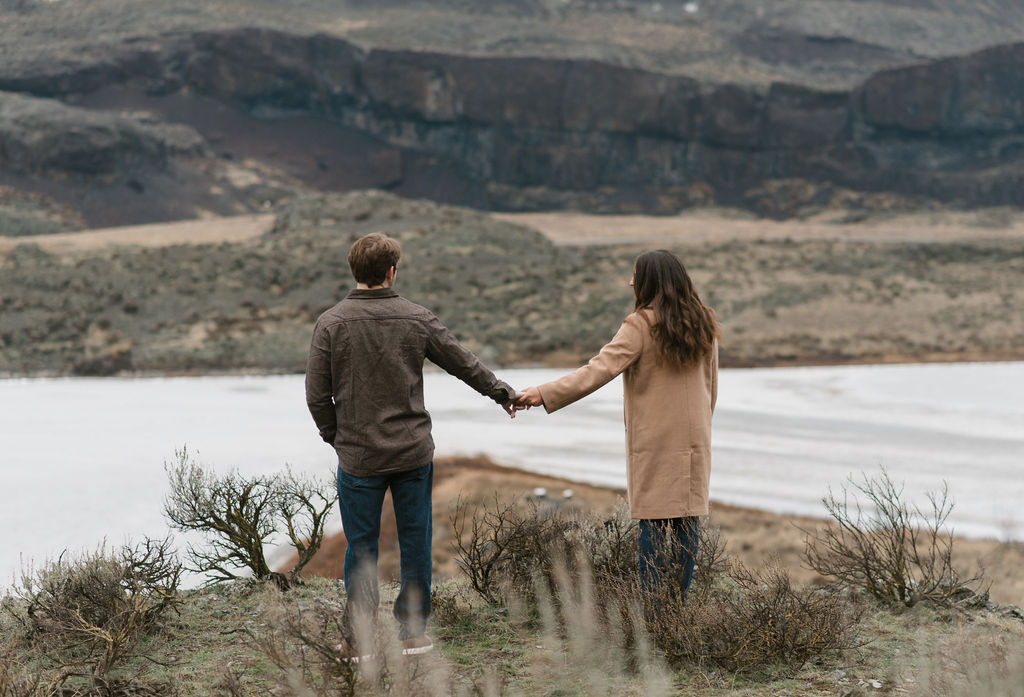 newly engaged couple holding hands and looking out at a frozen lake during their modern engagement pictures