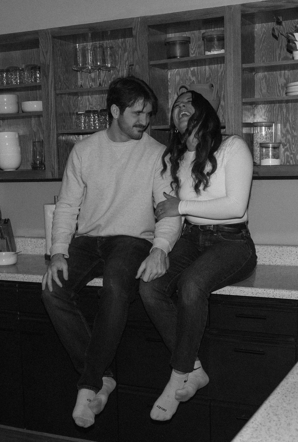 black and white of engaged couple laughing in their kitchen during engagement photos 