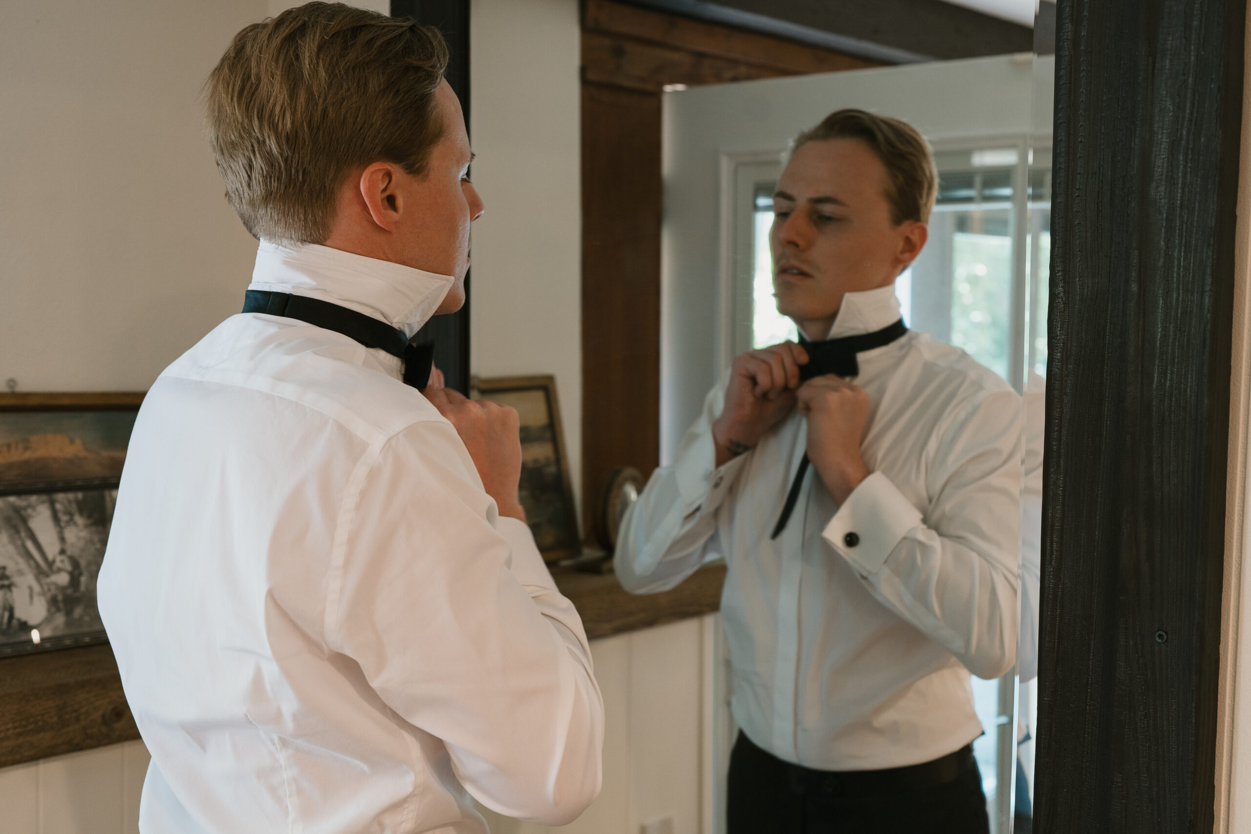 Groom putting on his bowtie while getting ready for his wedding