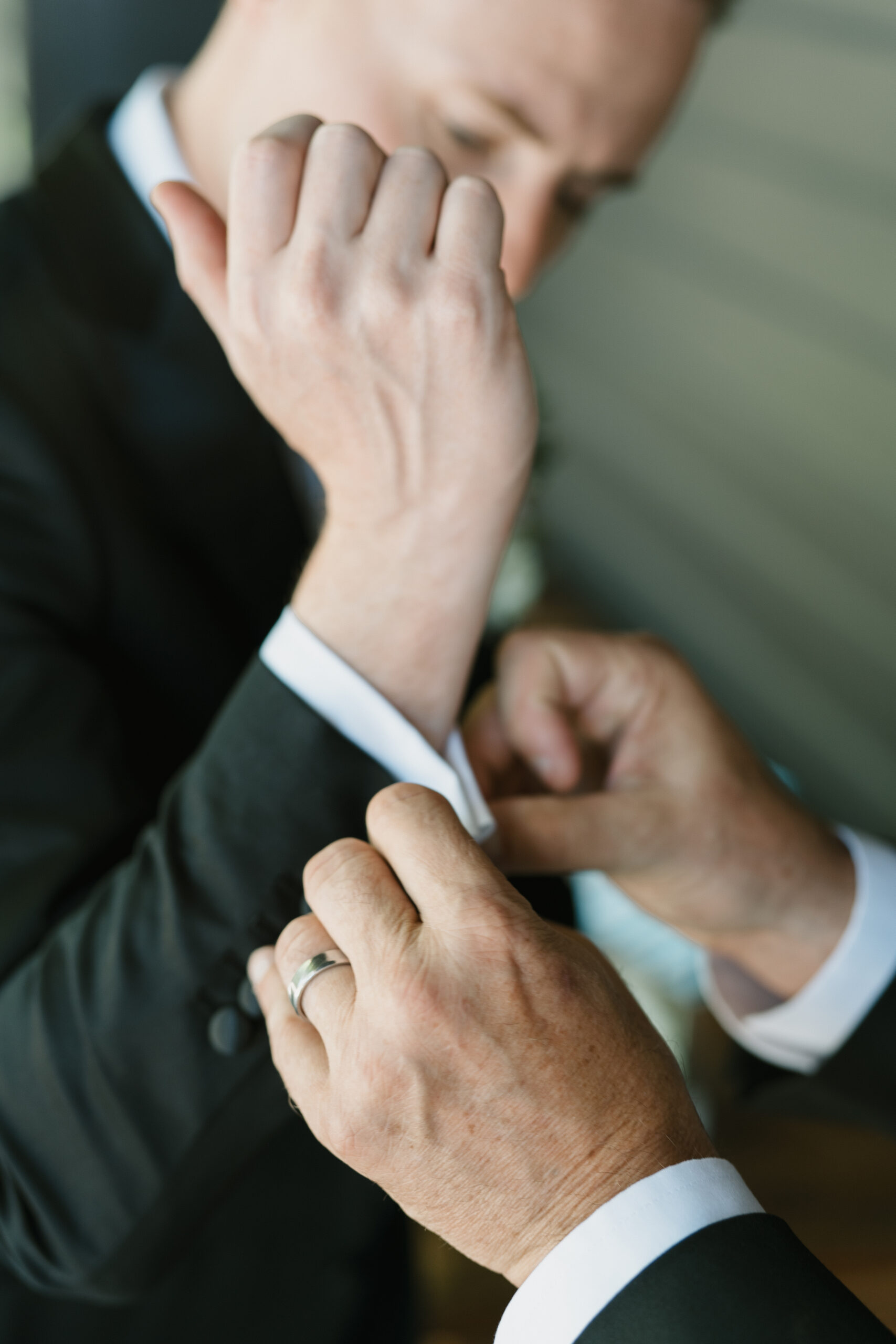 a close up of the groom's father putting on the groom's cufflinks