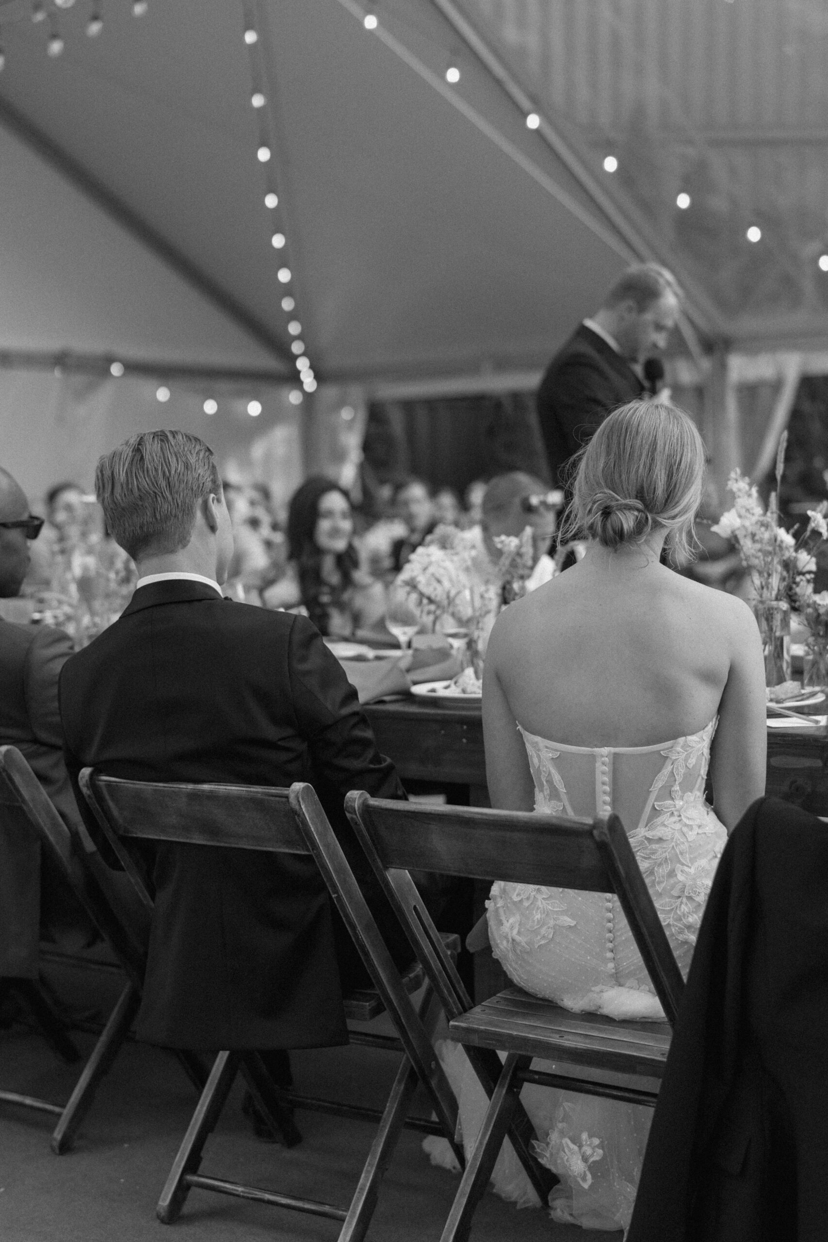 behind photo of the couple listening to toasts