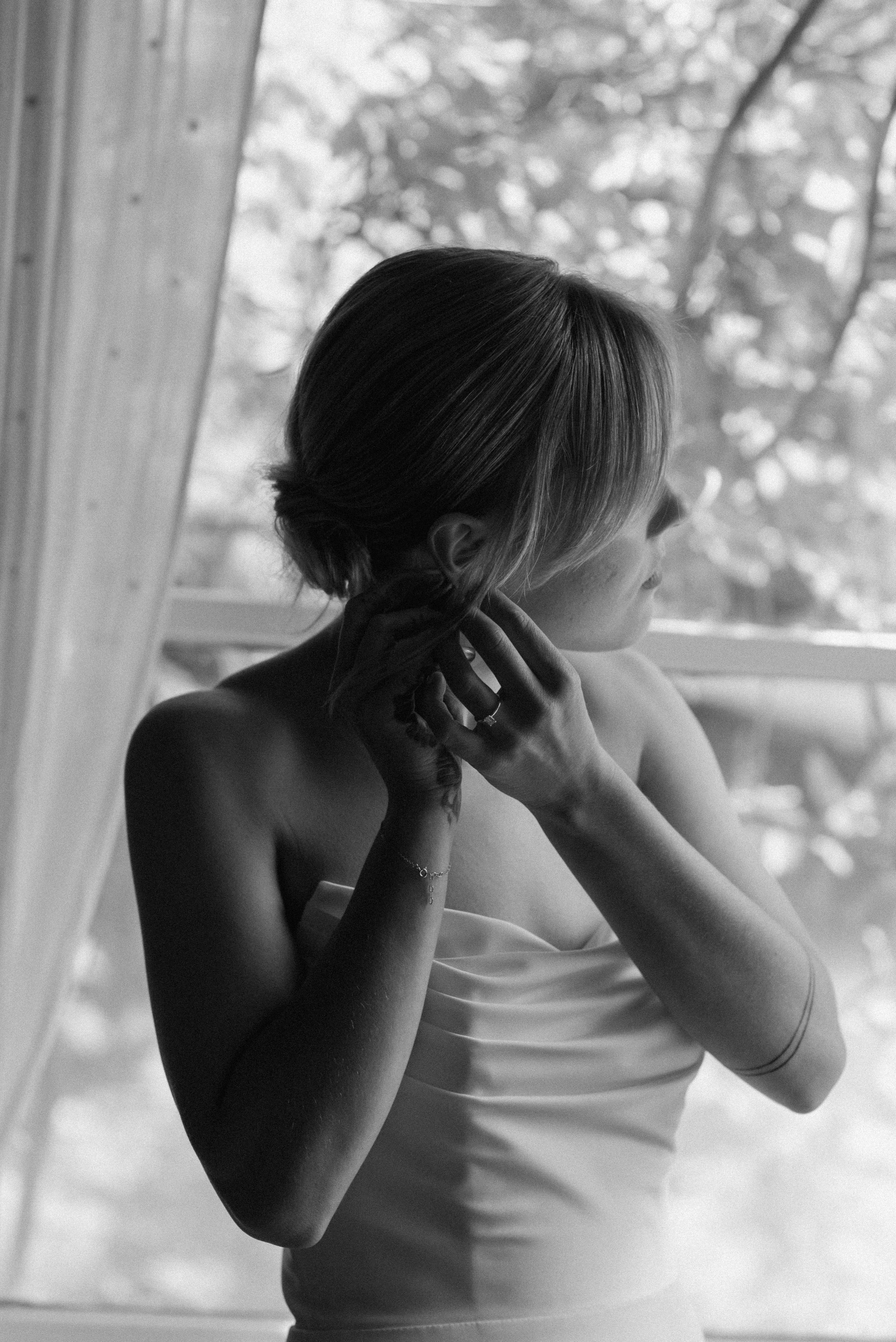 black and white of bride putting on her wedding earrings