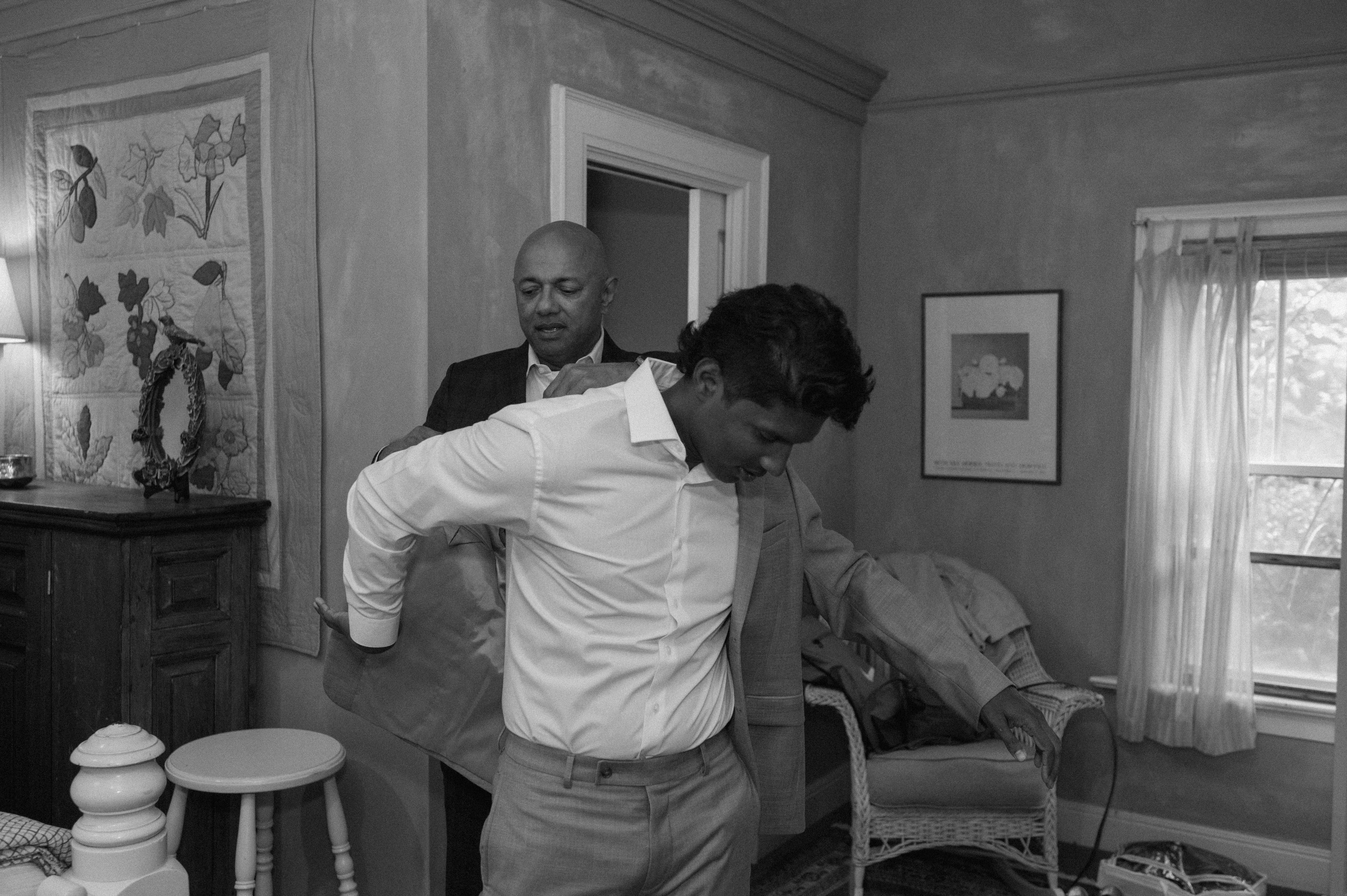 groom's father helping the groom put his suit jacket on for his wedding day